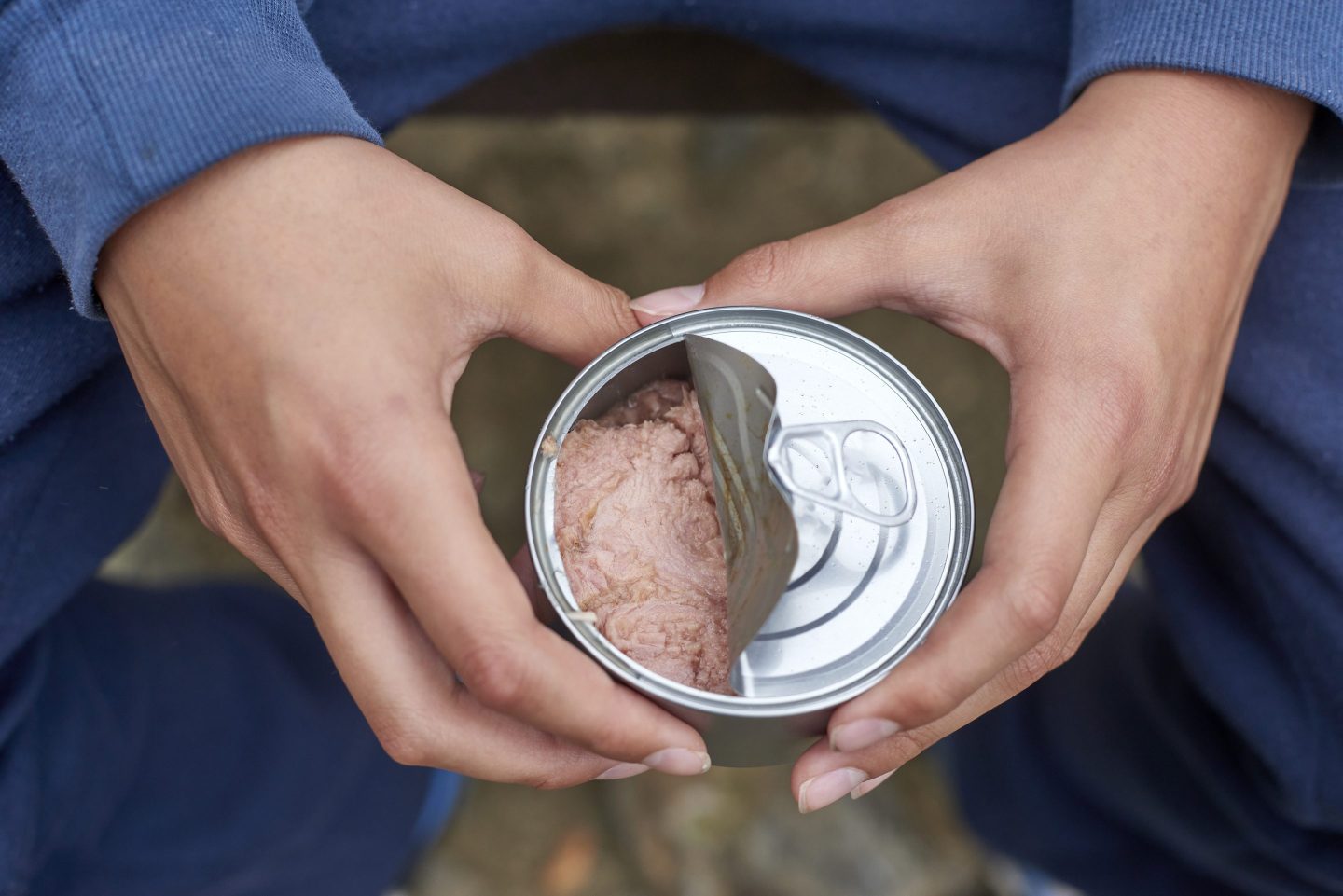 Close-up of a teenage boy&#039;s hands opening a can of tuna while camping or hiking in a wilderness area, demonstrating a quick and easy meal option for outdoor adventures